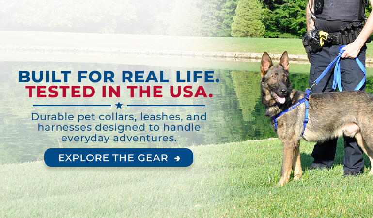 German Shepherd wearing a blue harness and leash stands on green grass beside a pond, held by a person partially visible at the edge of the frame. Overlay text reads: “Built for real life. Tested in the USA. Durable pet collars, leashes, and harnesses designed to handle everyday adventures.” A button says “Explore the gear.”