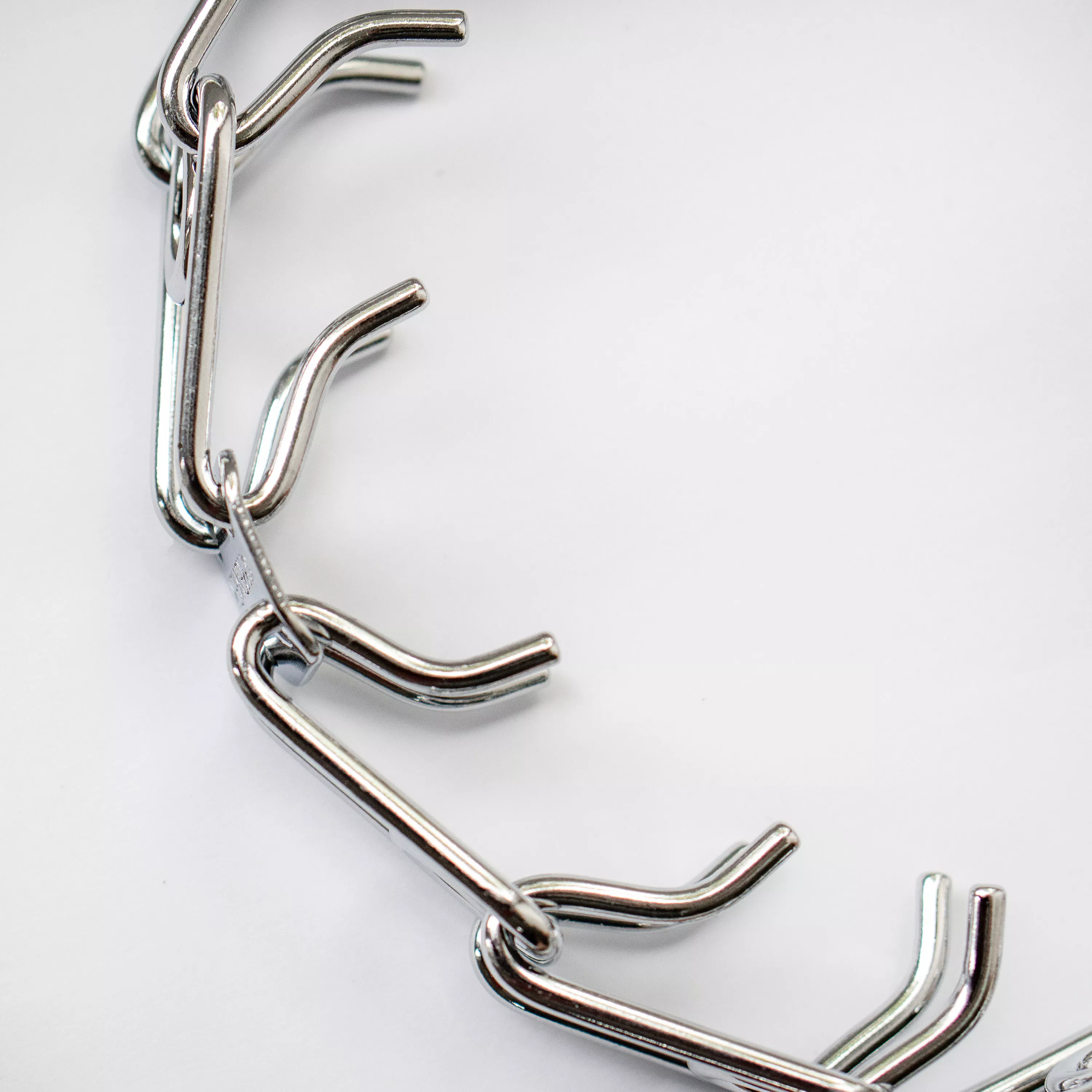 A close view of stainless steel prong links is shown against a white background. The links are shaped with smooth outward curves and inward-facing tips. The metal has a polished silver finish with smooth surfaces and rounded contours.