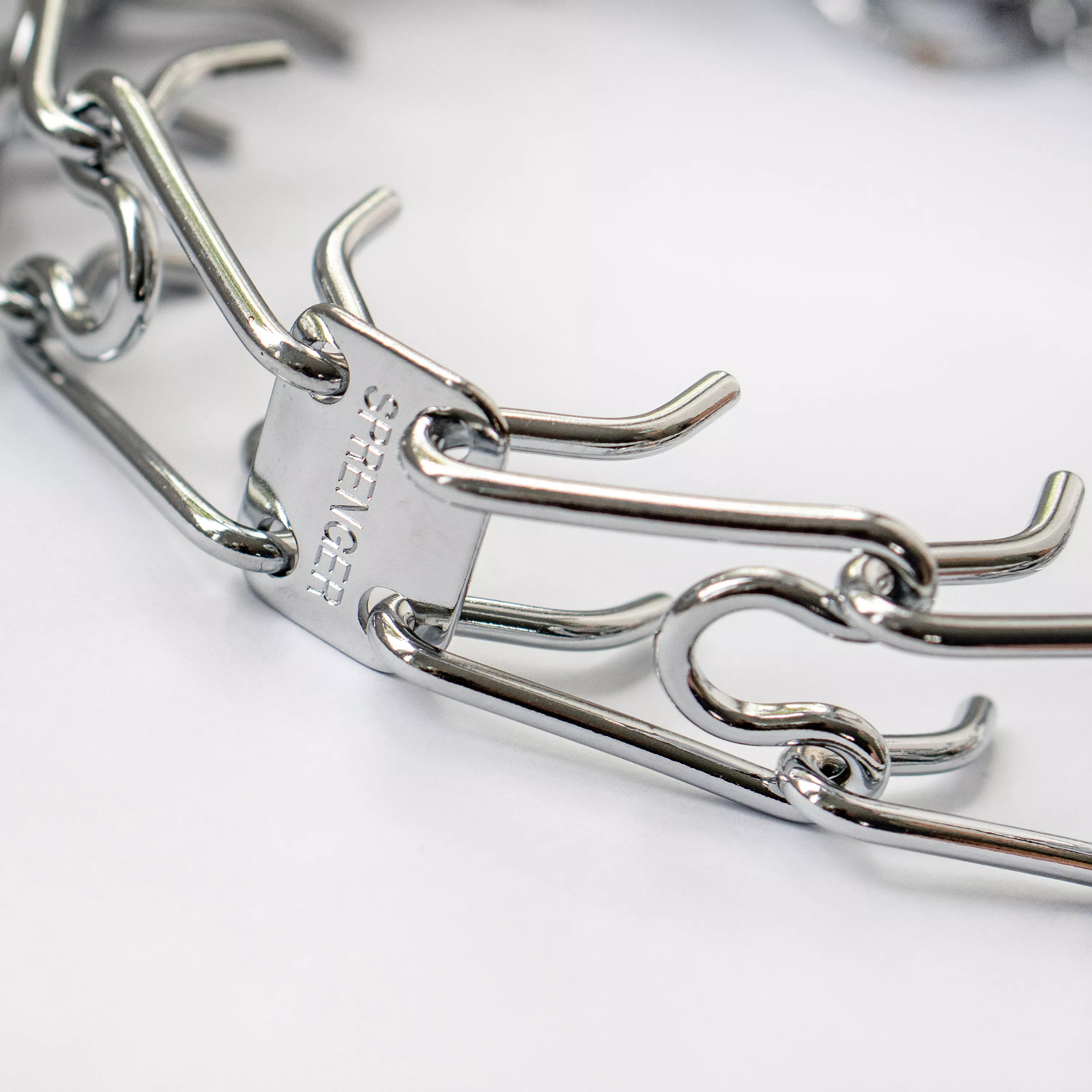 A product‑only photograph displays a stainless steel prong dog training collar against a solid white background. The collar is arranged in a curved shape, clearly showing the interlocking prongs, a latch mechanism, and smooth rounded link ends. The metal surface appears polished with a uniform silver finish.