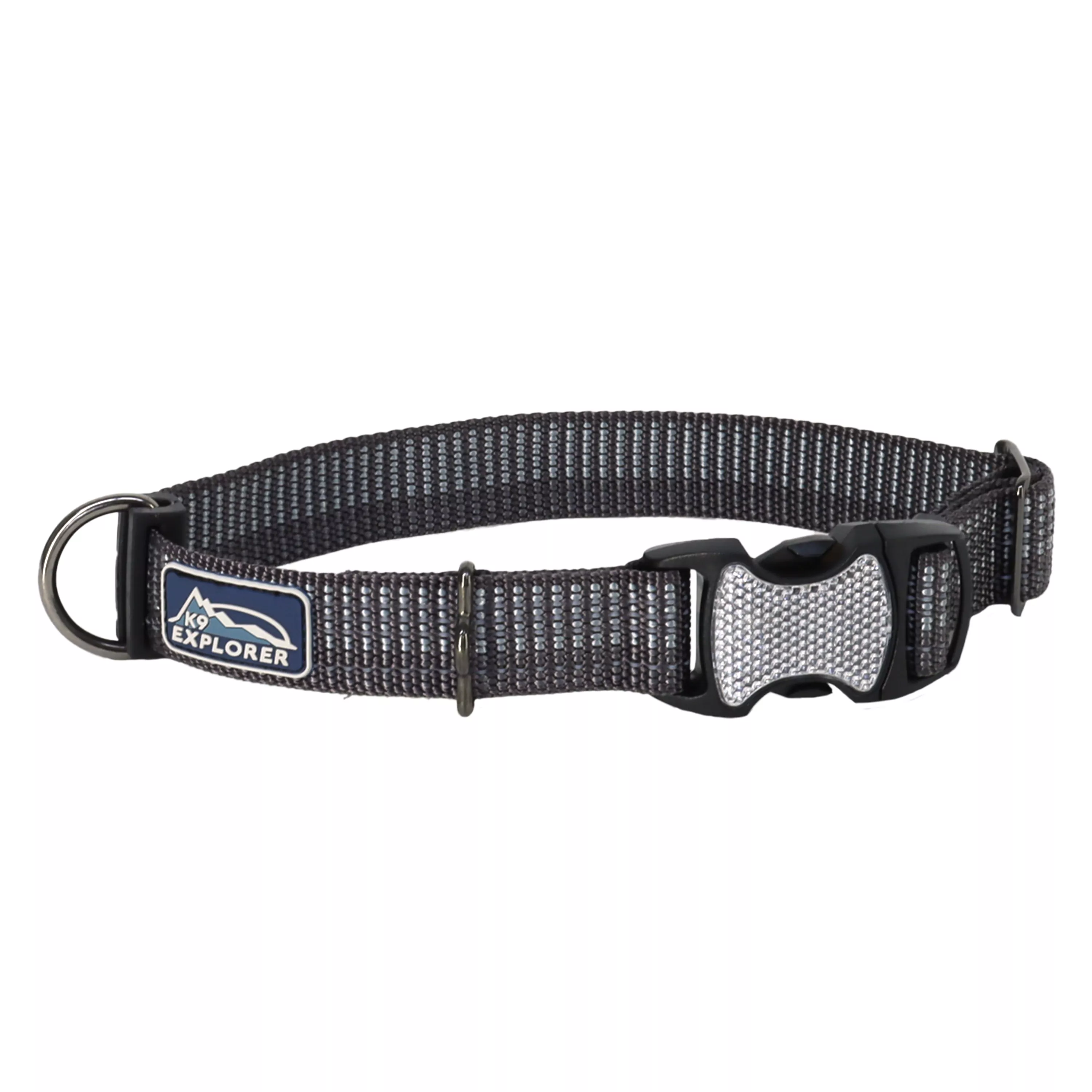 A product‑only photograph displays an adjustable reflective dog collar against a solid white background. The collar is made of black flat woven material with integrated reflective stitching running lengthwise. Gray plastic hardware includes a side‑release buckle and an adjustment slider. A black metal D‑ring is attached along the strap. A woven fabric label on the collar displays printed text reading “K9 EXPLORER.”