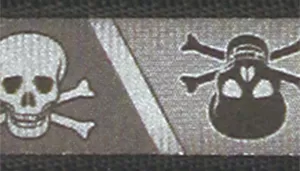 A swatch displays reflective woven fabric with a skull and crossbones pattern. The background appears medium gray with reflective properties. White skull and crossbones icons repeat across the surface. A black fabric border runs along the top and bottom edges.