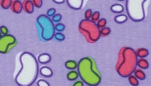 A swatch showing a whimsical pattern of multicolored paw prints on a lavender background. The paws appear in lime green, turquoise, bright pink, and white, each outlined in black. Small doodle accents fill the spaces between paws. The surface is smooth and evenly printed with vibrant color contrast.