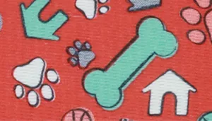 A swatch showing a playful dog‑themed pattern printed on a bright red background. Scattered across the surface are cartoon‑style illustrations of white dog bones, teal paw prints, and small house icons outlined in black. The motifs are casually spaced with soft, rounded shapes and clean print lines. The red base is saturated and uniform, giving strong contrast to the lighter imagery.