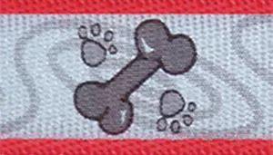A swatch shows reflective woven fabric with a repeating red paw print and bone pattern. The background fabric appears light gray with reflective qualities. Red paw prints and bone shapes repeat across the surface. A solid red fabric border runs along the top and bottom edges.