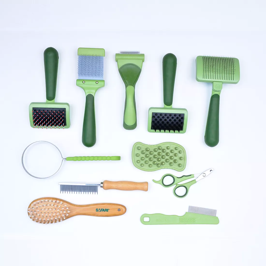 A set of pet grooming tools is displayed on a white background. The tools vary in shape and size and include brushes, combs, nail tools, and de‑shedding tools in coordinated shades of pale and dark green. The arrangement shows multiple handle styles and grooming head types.