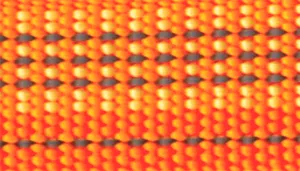 A swatch displaying a tightly woven textile in warm, desert‑inspired colors. The pattern consists of repeating vertical threads in bright orange, mustard yellow, and deep red, creating a small, grid‑like texture. Gray reflective threads appear intermittently within the weave, adding contrast and depth. The surface has a rugged, structured, outdoor‑gear aesthetic.