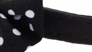 A swatch featuring a playful dotted pattern on a black background. The visible portion includes white oval and circular dots printed onto black fabric. A black strap runs along the edge of the swatch, showing the material’s binding and stitch details.